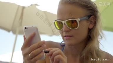 年轻的微笑的金发女人使用智能手机与笔在炎热的夏天，手和移动反映在太阳镜